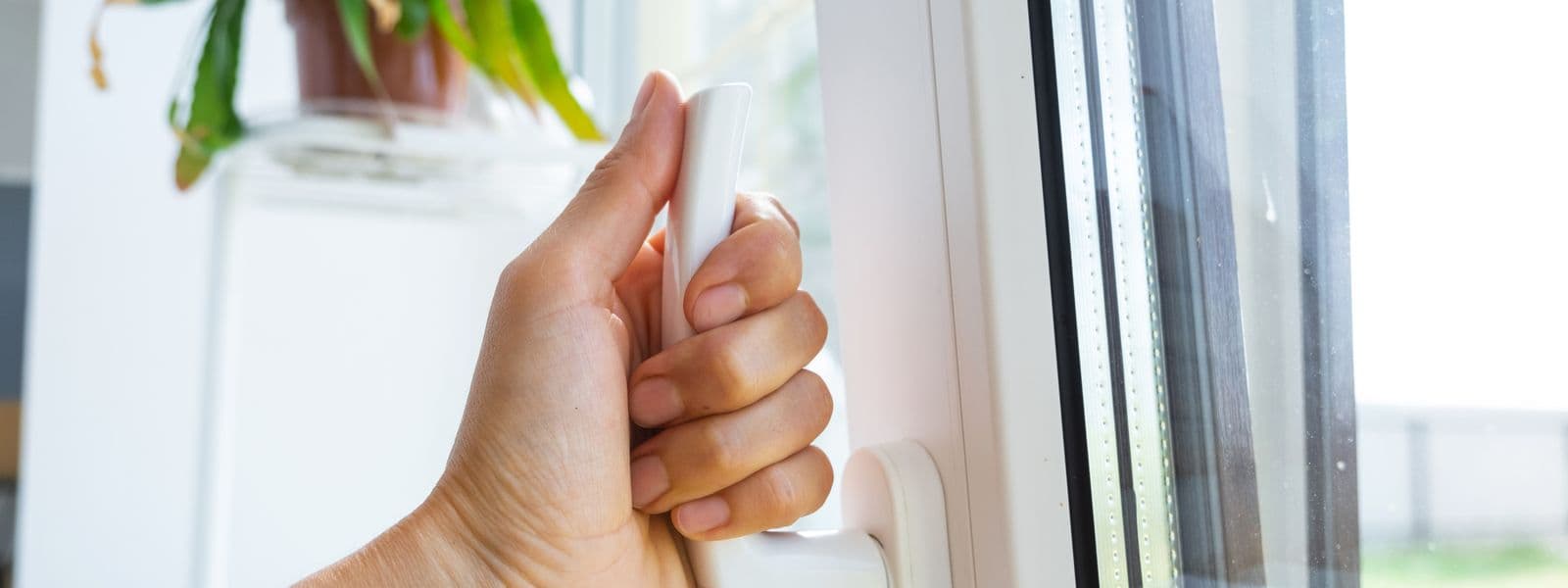 Hand am Griff eines Kunststofffensters in einer Wohnung